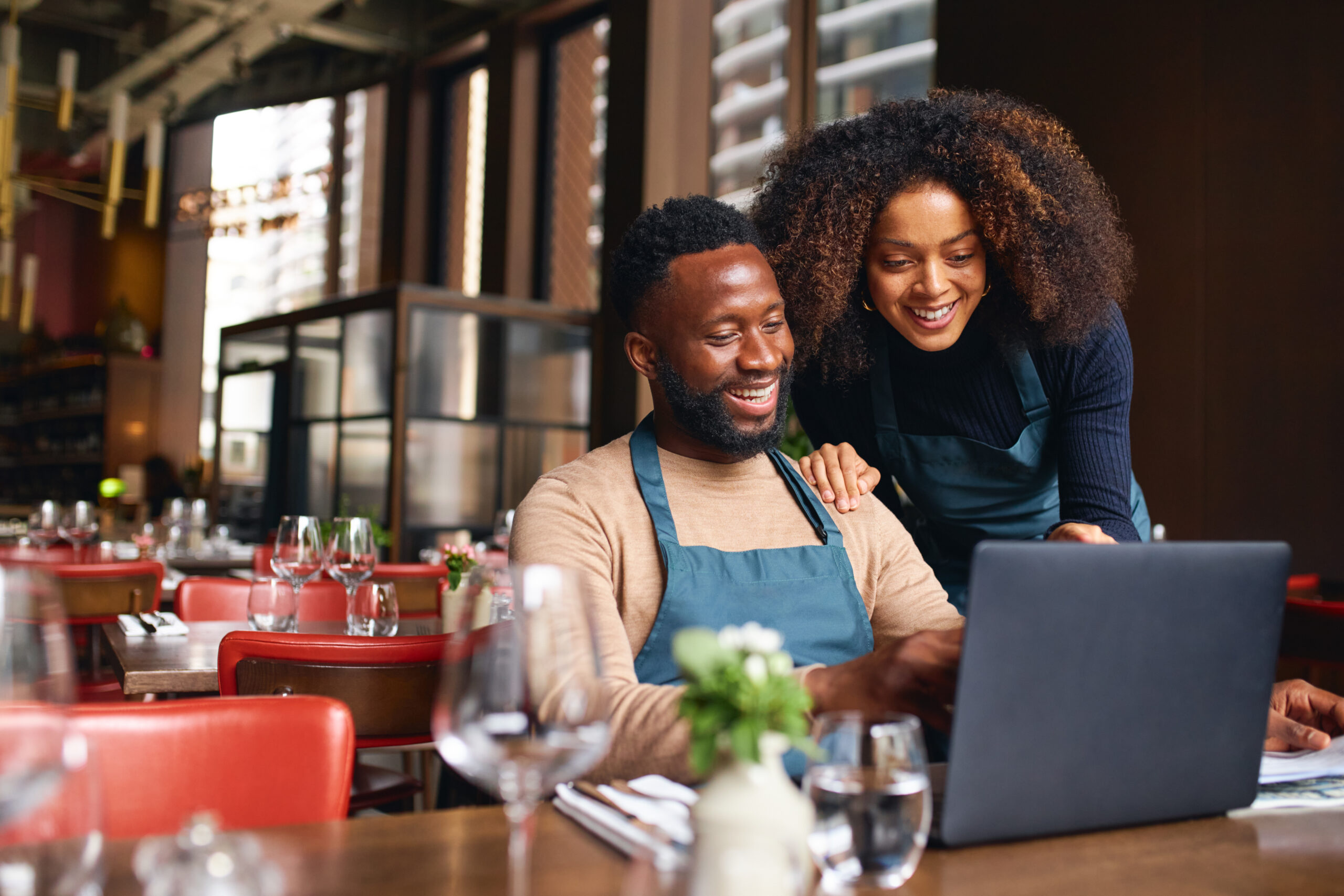 Small business couple looking at laptop with restaurant in background